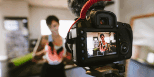 Close-up of a DSLR camera recording a woman holding a pair of bright athletic shoes, creating short-form video content in a casual indoor setting.