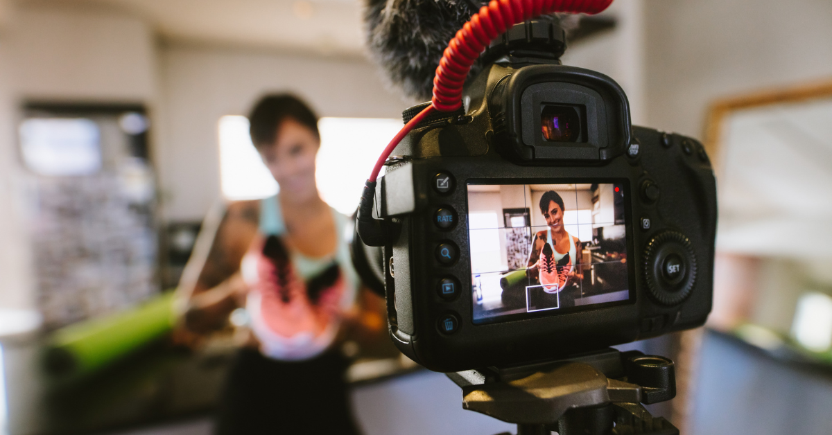 Close-up of a DSLR camera recording a woman holding a pair of bright athletic shoes, creating short-form video content in a casual indoor setting.